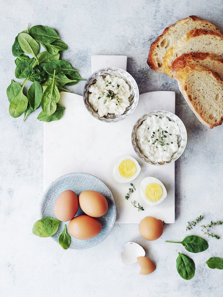 Ingredients placed on a cutting board: eggs, ricotta & cottage cheese, toast & baby spinach leaves