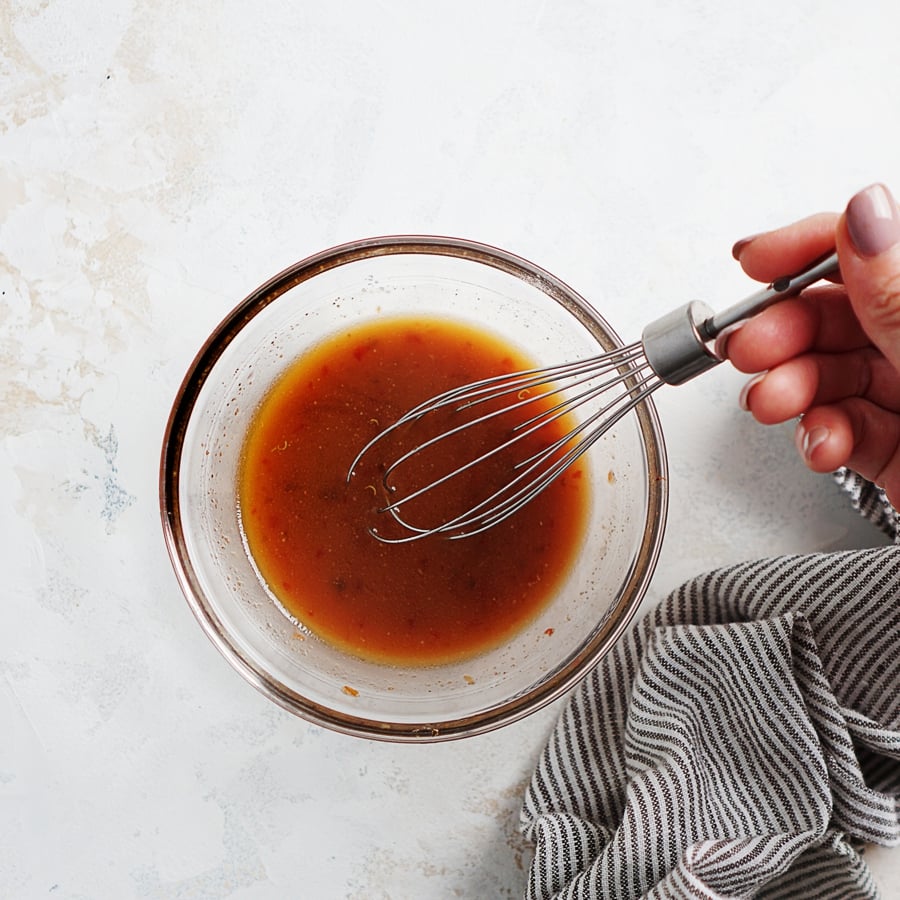 A small bowl filled with Asian sauce being whisked by a hand. 
