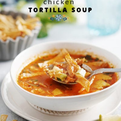 A white bowl of sopa de tortilla with a spoon