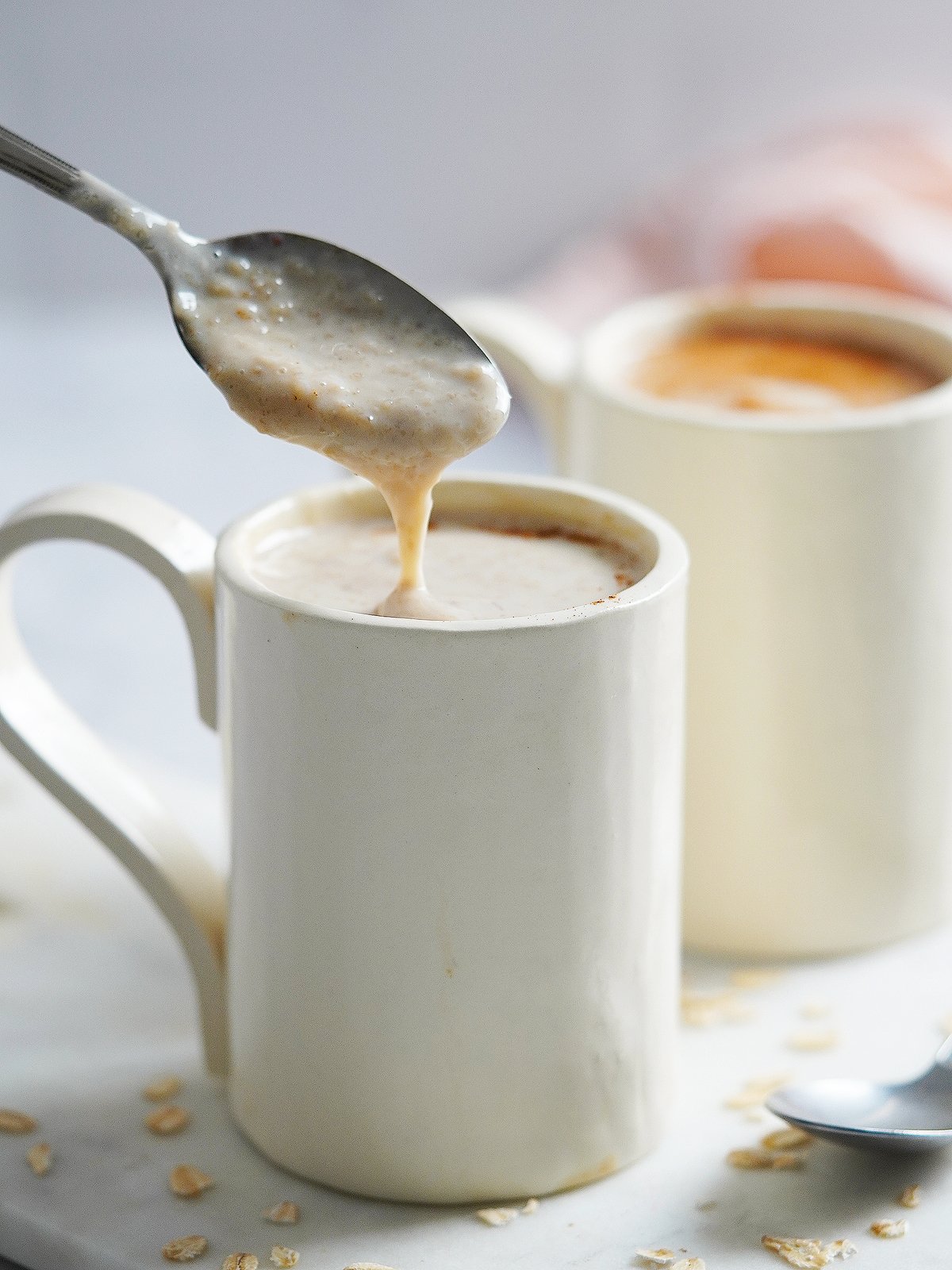 A white mug with a spoon dripping some oatmeal drink