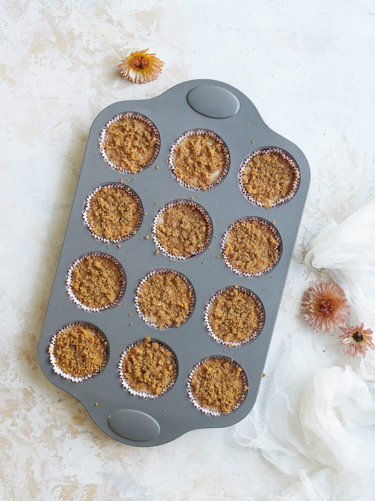 A 12 muffin pan showing the cinnamon crumbs on top of the batter