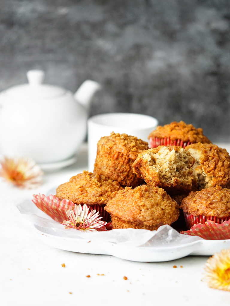 A plate with banana crumb muffins and a tea pot in the background