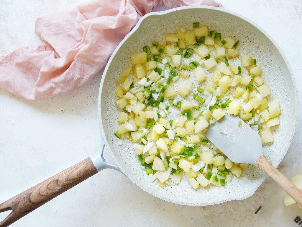 A skillet with potatoes, onions & green chiles. pink kitchen towel on the side