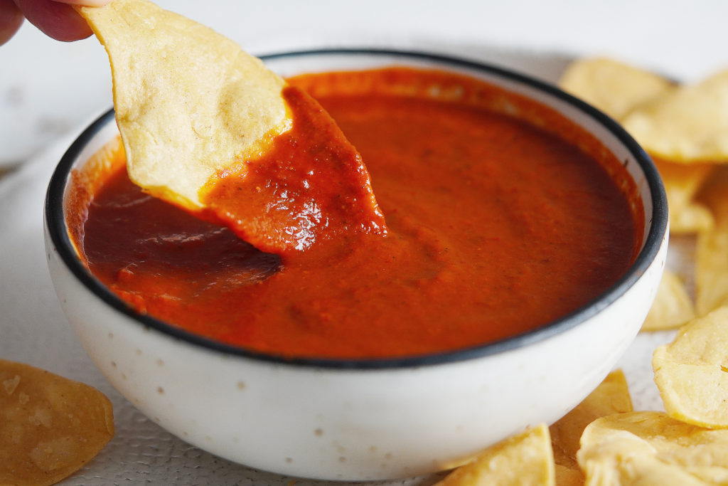 A bowl of salsa with a tortilla chip dipping into it.