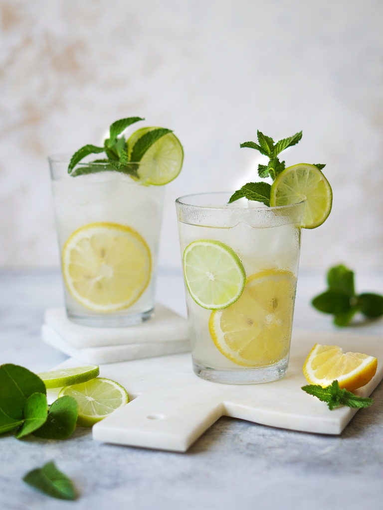 Two glasses filled with a clear drink and lemons & limes as garnish