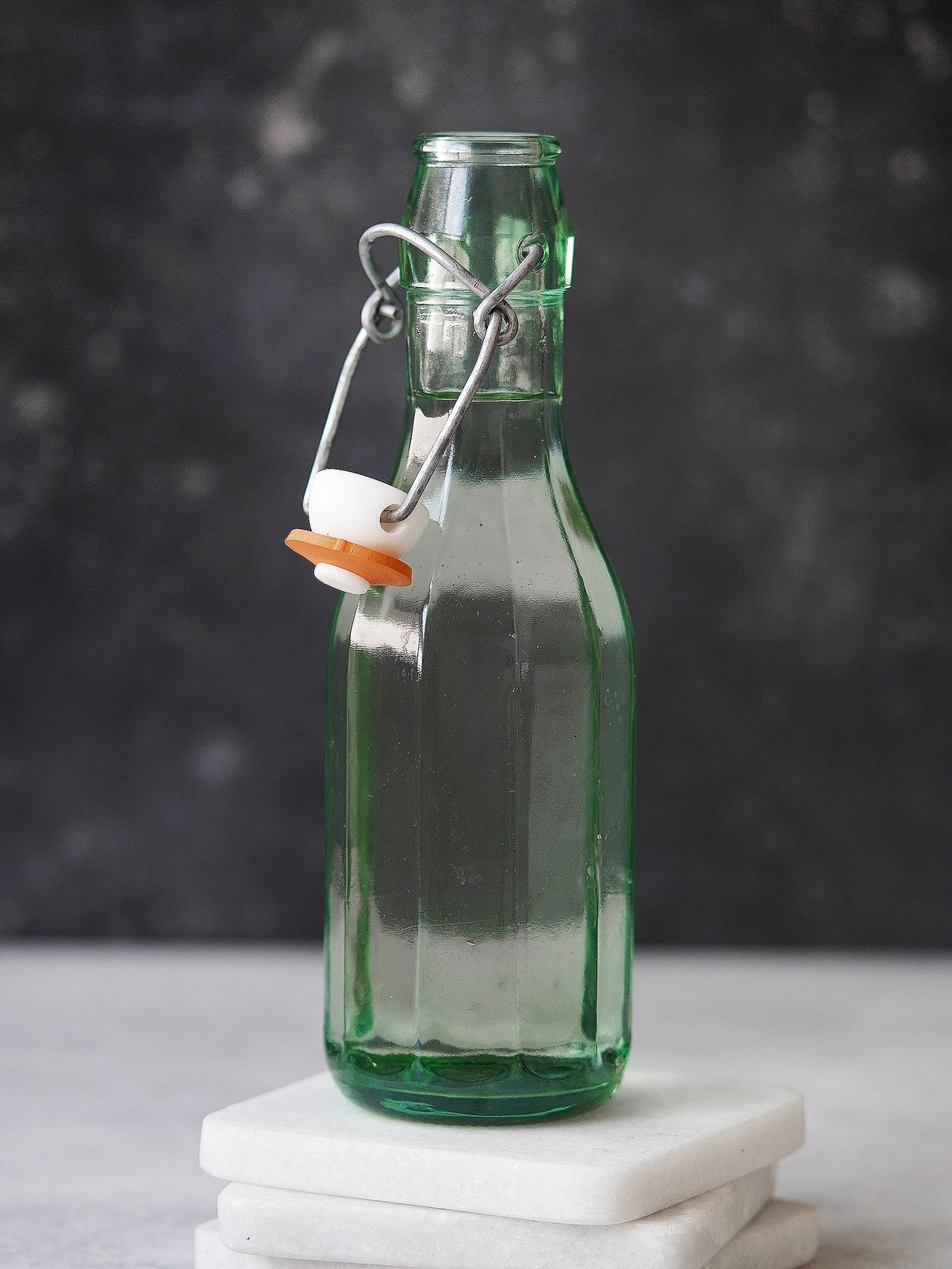 A green glass bottle with clear simply syrup. Dark background