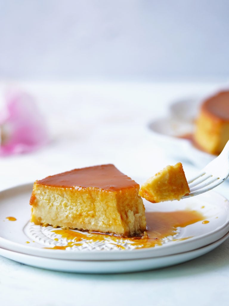 A slice of flan on a dessert plate and a white fork on the side.