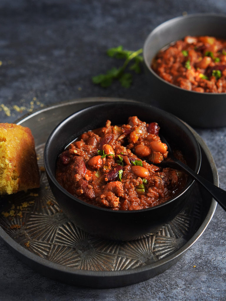 Beef Chili in a black bowl with corn bread on the side