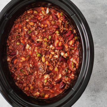 A crockpot bowl with ground beef, spices, beans, celery, bell peppers & onions. All mixed in.