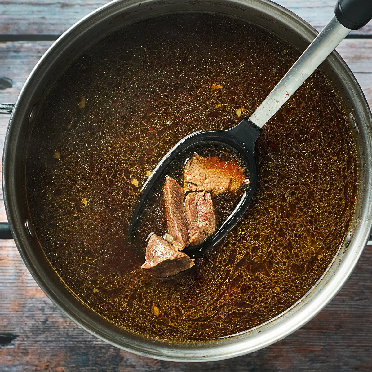 Image of beef in a large pot cooked in red broth