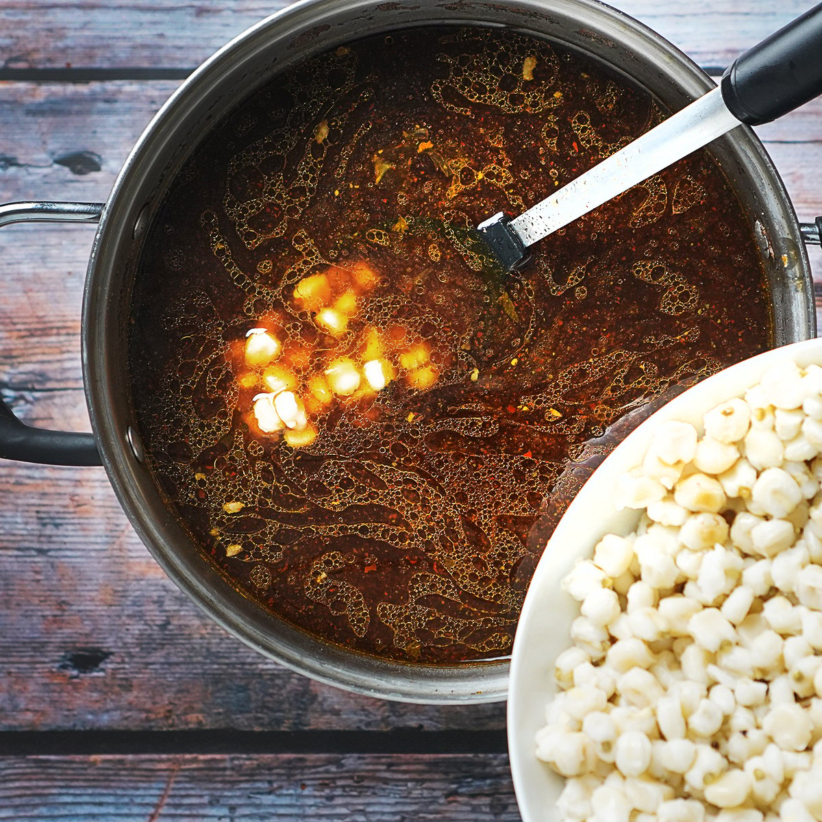Adding hominy to a a large pot with cooked beef