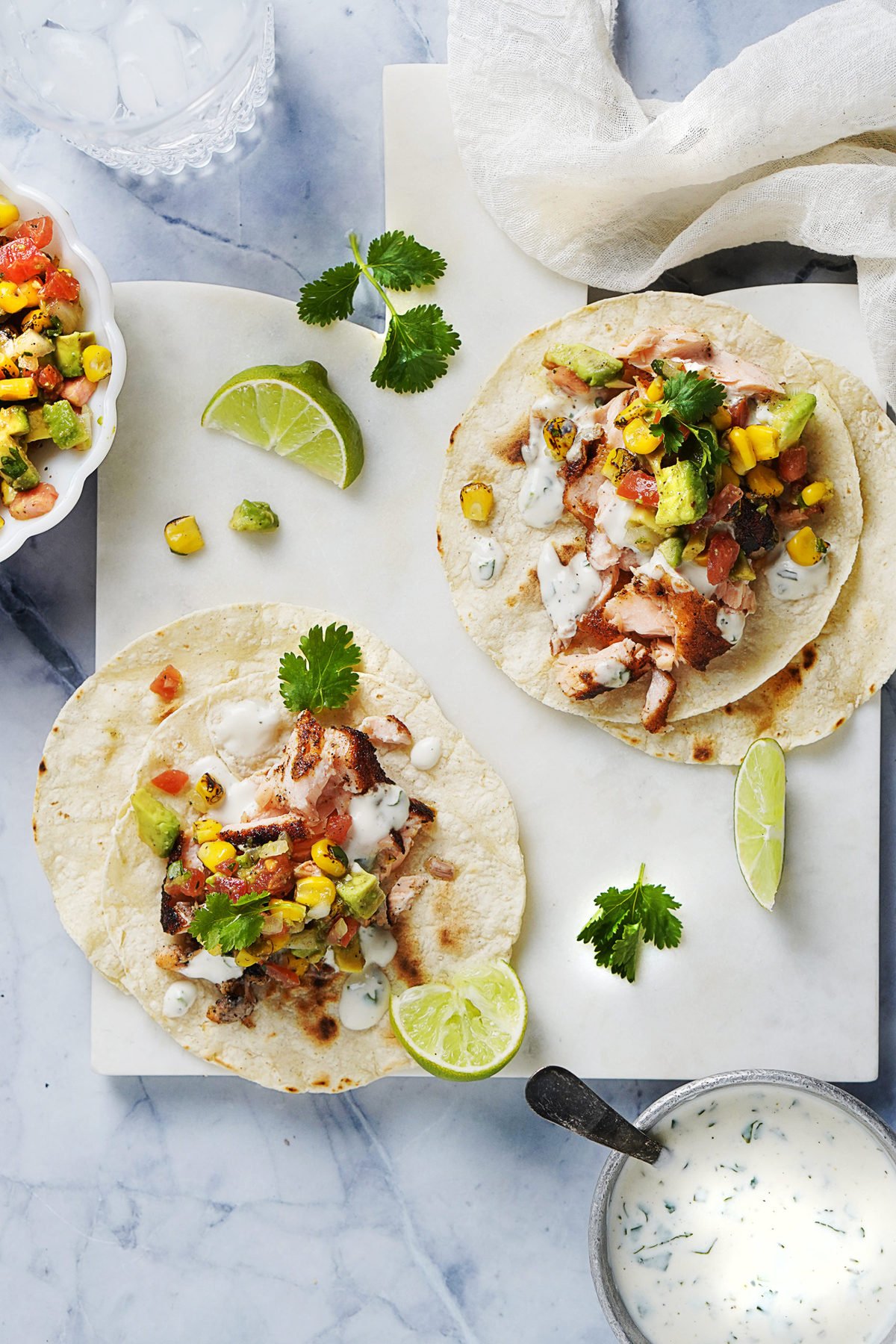 Blackened Salmon Tacos on a white board with corn salsa on the side and crema in a small bowl