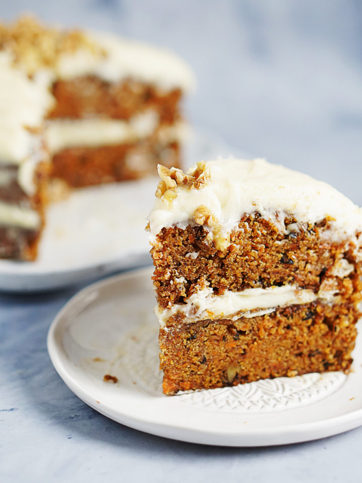 a slice of carrot cake and the whole cake in the background