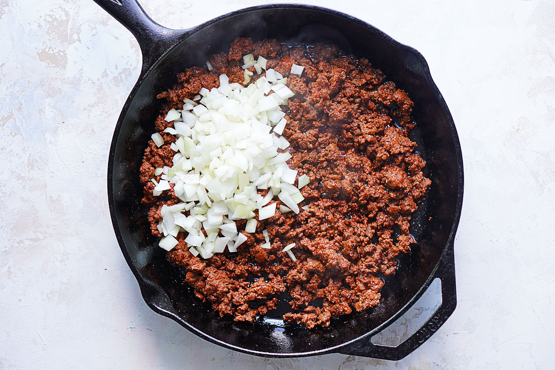 Adding chopped onions to cooked chorizo in a skillet