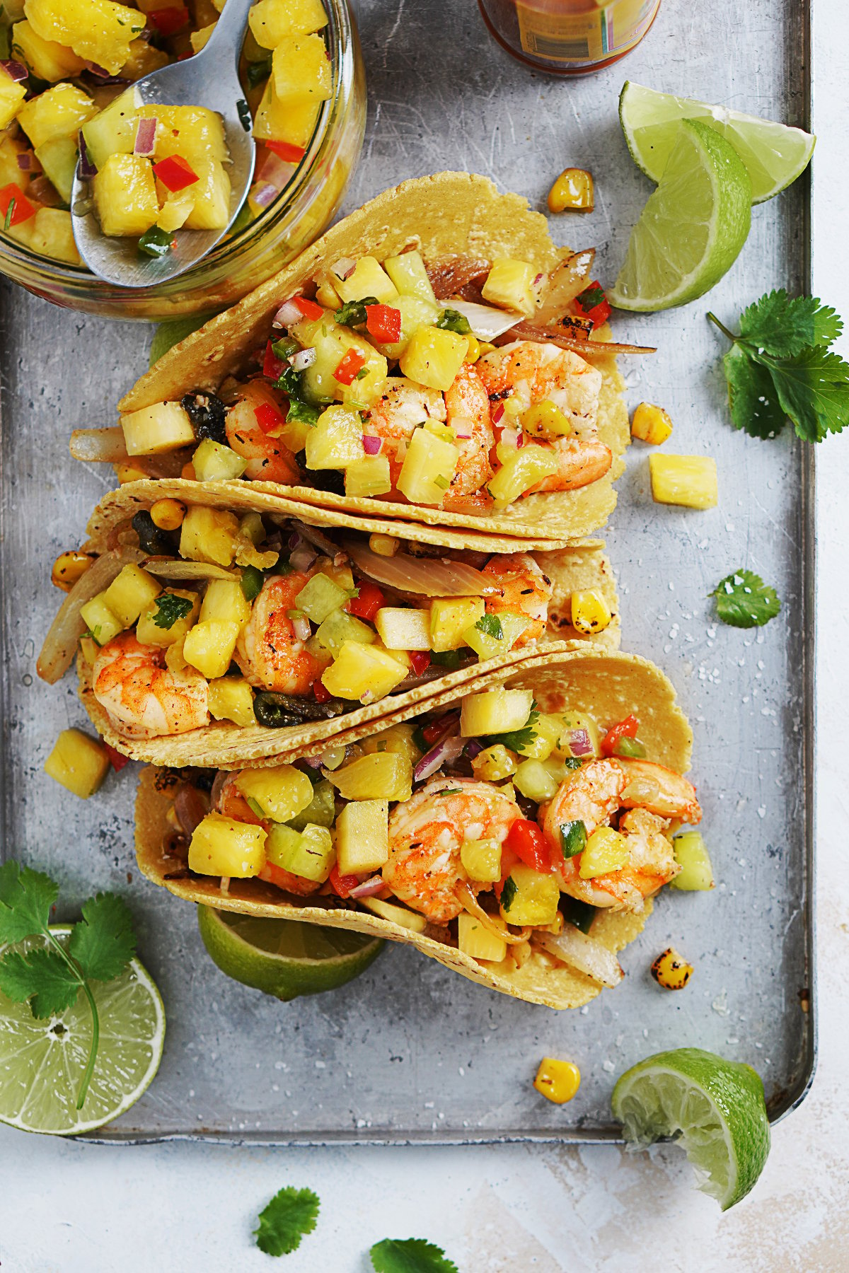 3 tacos with shrimp, onions, peppers and corn with pineapple salsa on top.