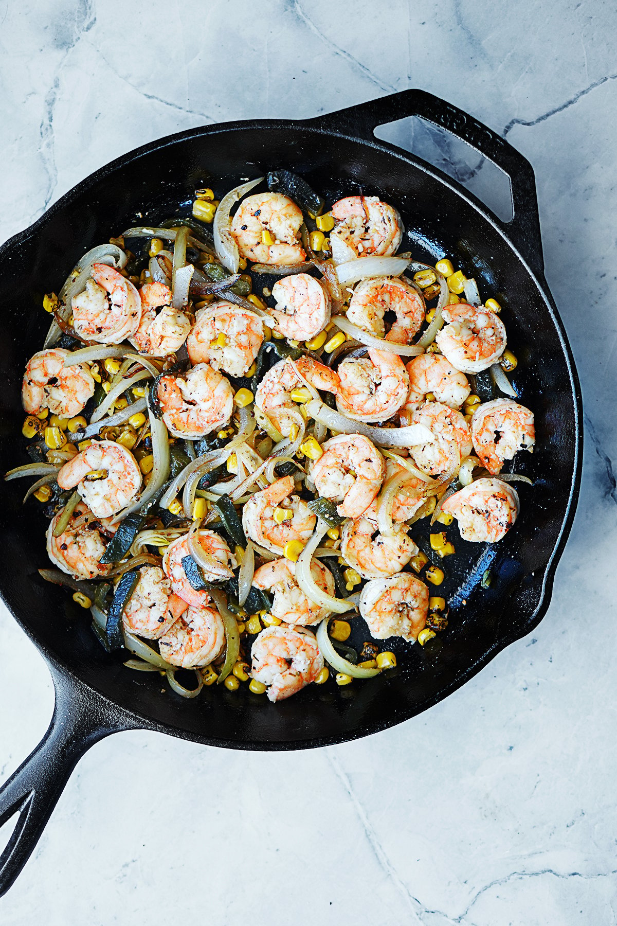 A black skillet with cooked shrimp, onions, corn and poblano peppers