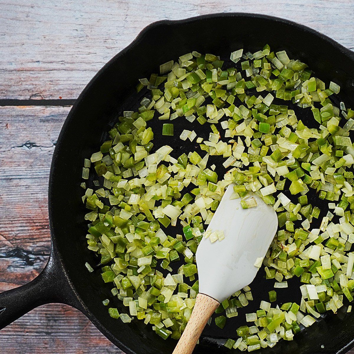 Sauteing onions and green bell peppers on an iron skillet