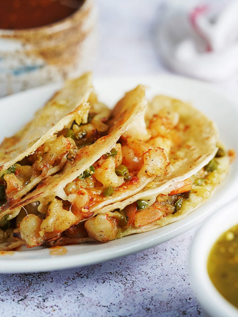Three tacos with shrimp and salsas on the side.