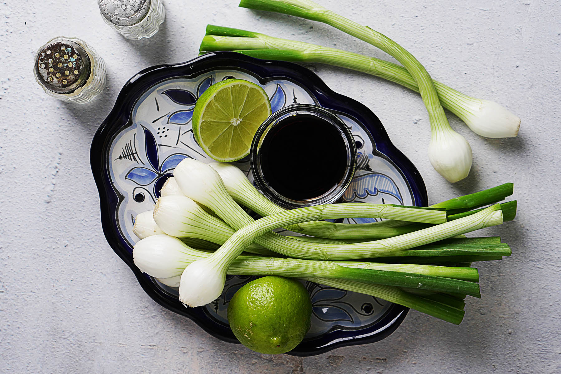 Raw green onions on a blue plate with soy sauce and a lime on the side