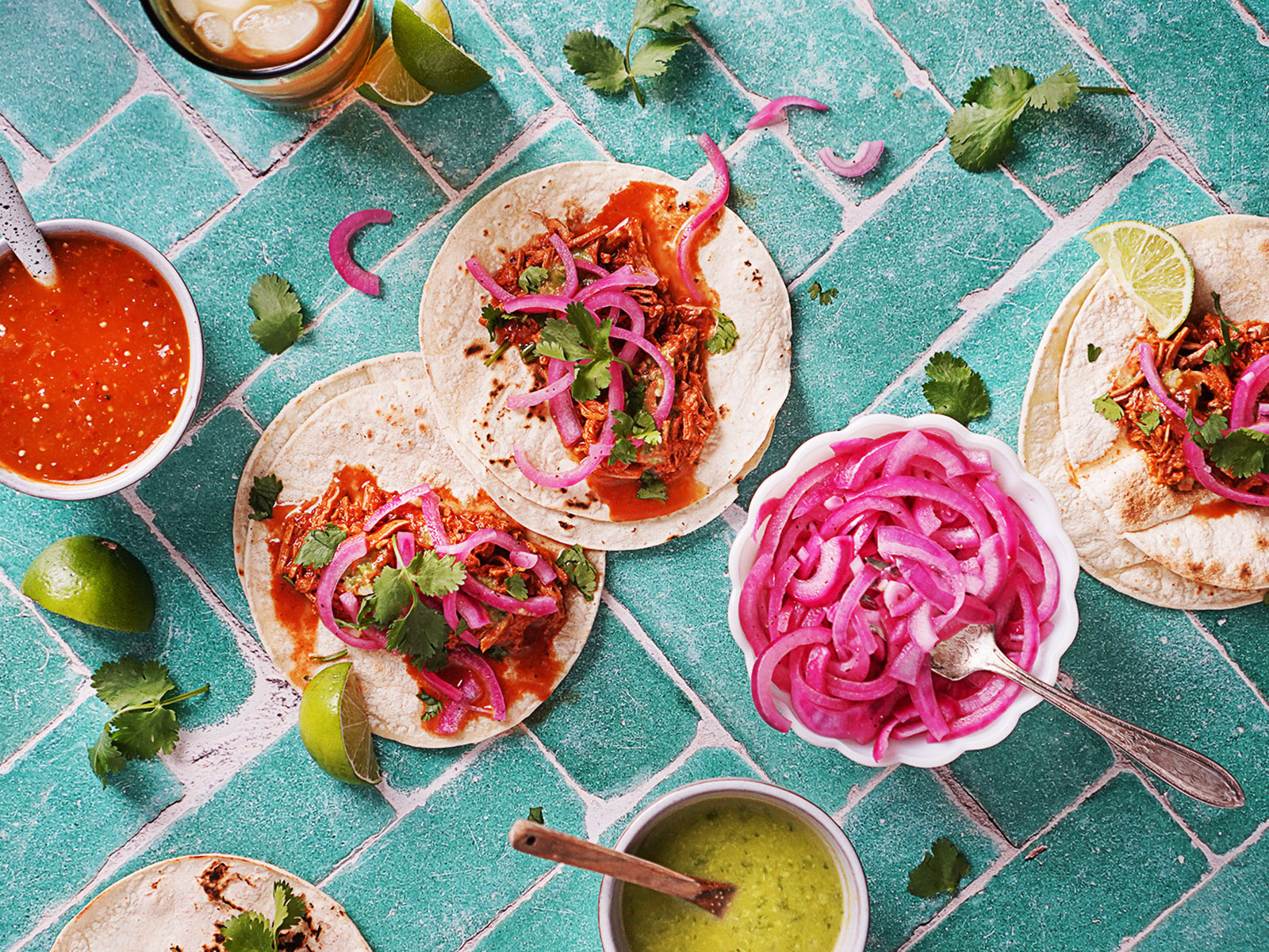 3 cochinita pibil tacos on a green title table with salsas on small bowls