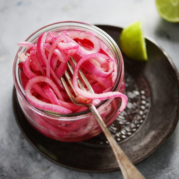 sliced red onions in a small glass jar with a fork