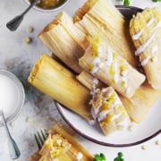 A large plate with corn tamales still wrapped in husk