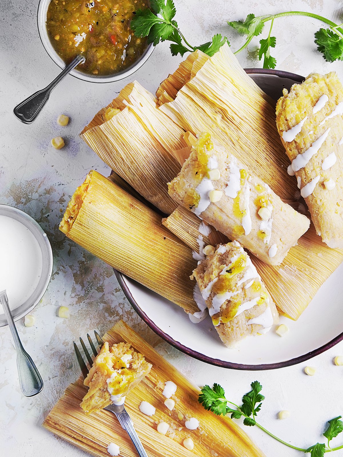 A large plate with corn tamales de elote still wrapped in husk