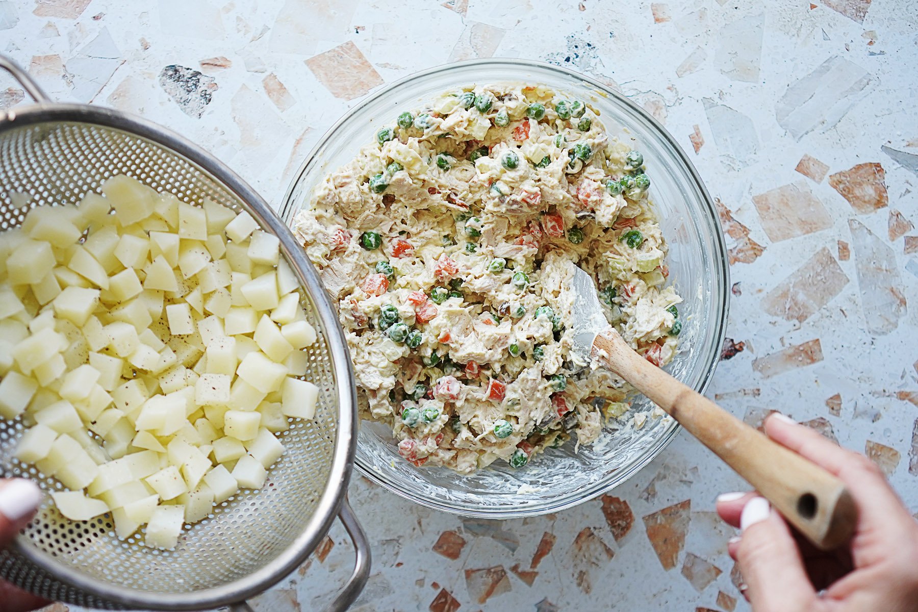 A bowl with chicken salad and boiled potatoes on the side in a colander
