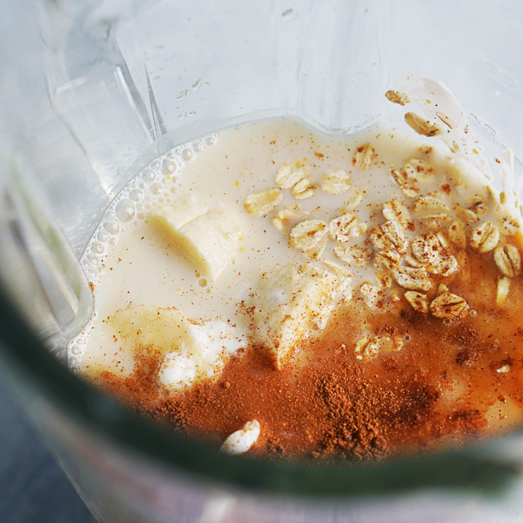 A blender's glass with milk, oatmeal, cinnamon and bananas