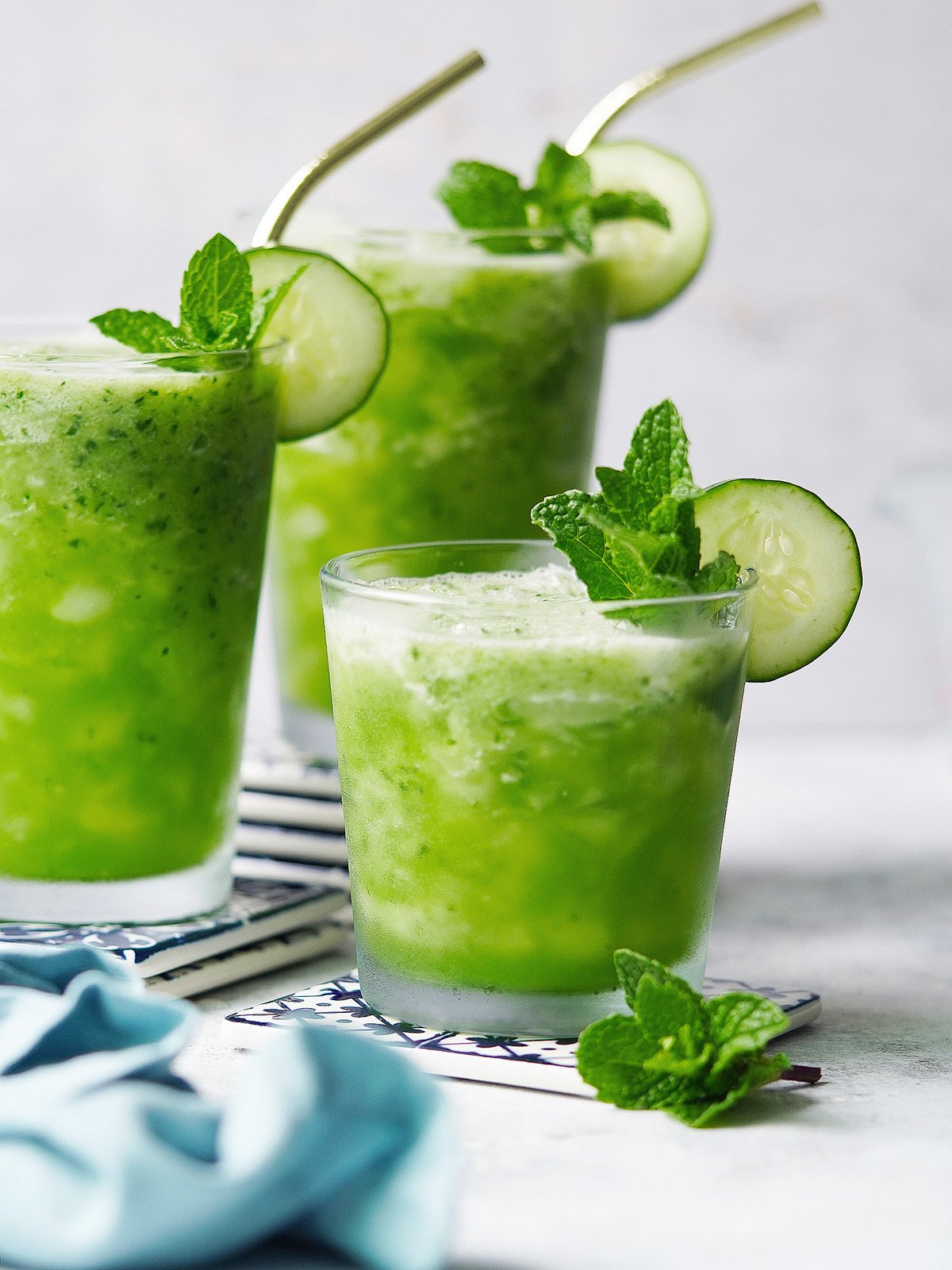 3 glasses with Agua De Pepino garnished with a slice of cucumber and mint