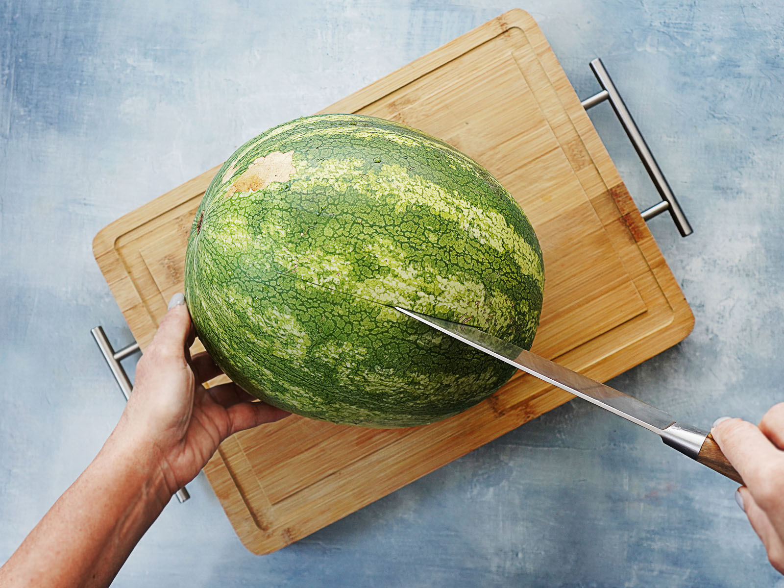 Two hands cutting a large watermelon with a knife