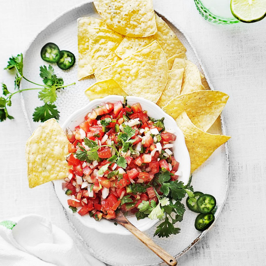 A white bowl with salsa fresca and tortilla chips on the side