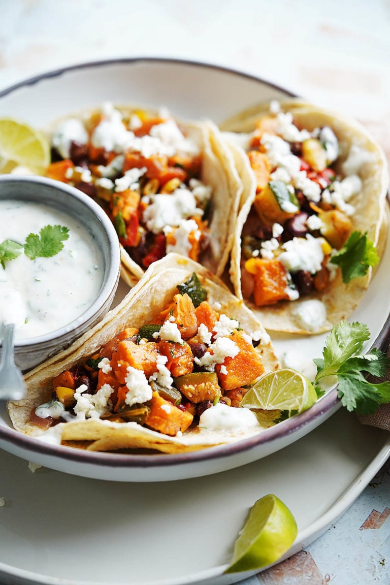 3 vegetable tacos on a white plate garnished with queso fresco