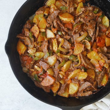 A skillet with cooked steak, potatoes and chiles