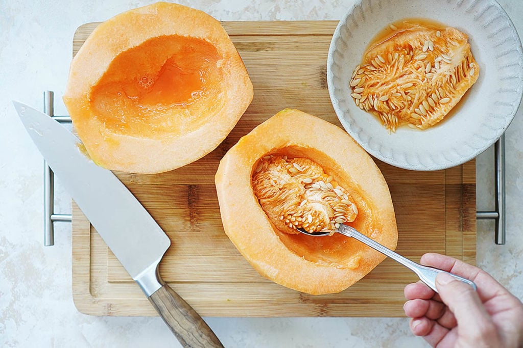 Scooping the seeds out of a cantaloupe with a spoon.