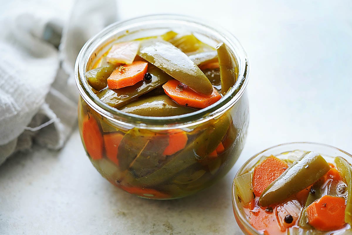 A glass jar and small bowl with pickled peppers and carrots.