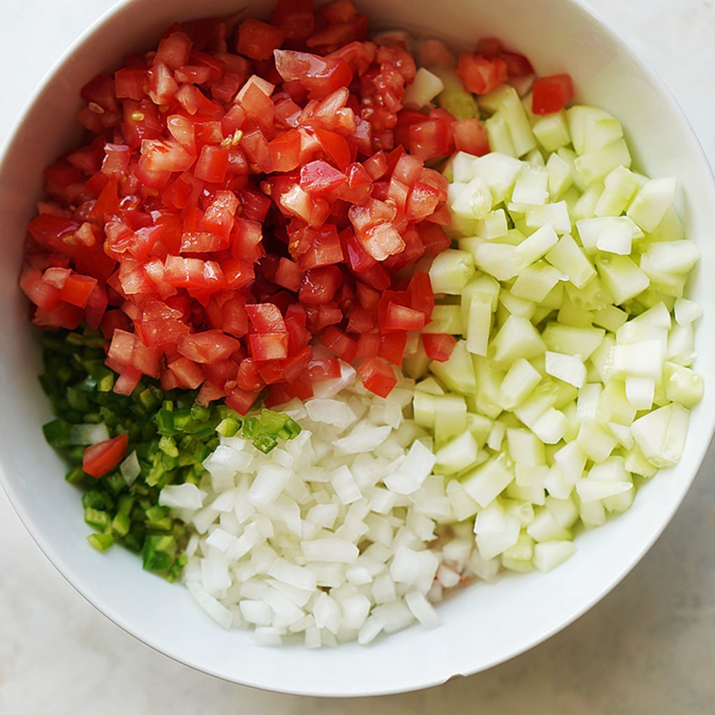 A large white bowl with chopped onions, cucumber, tomato and jalapeños.