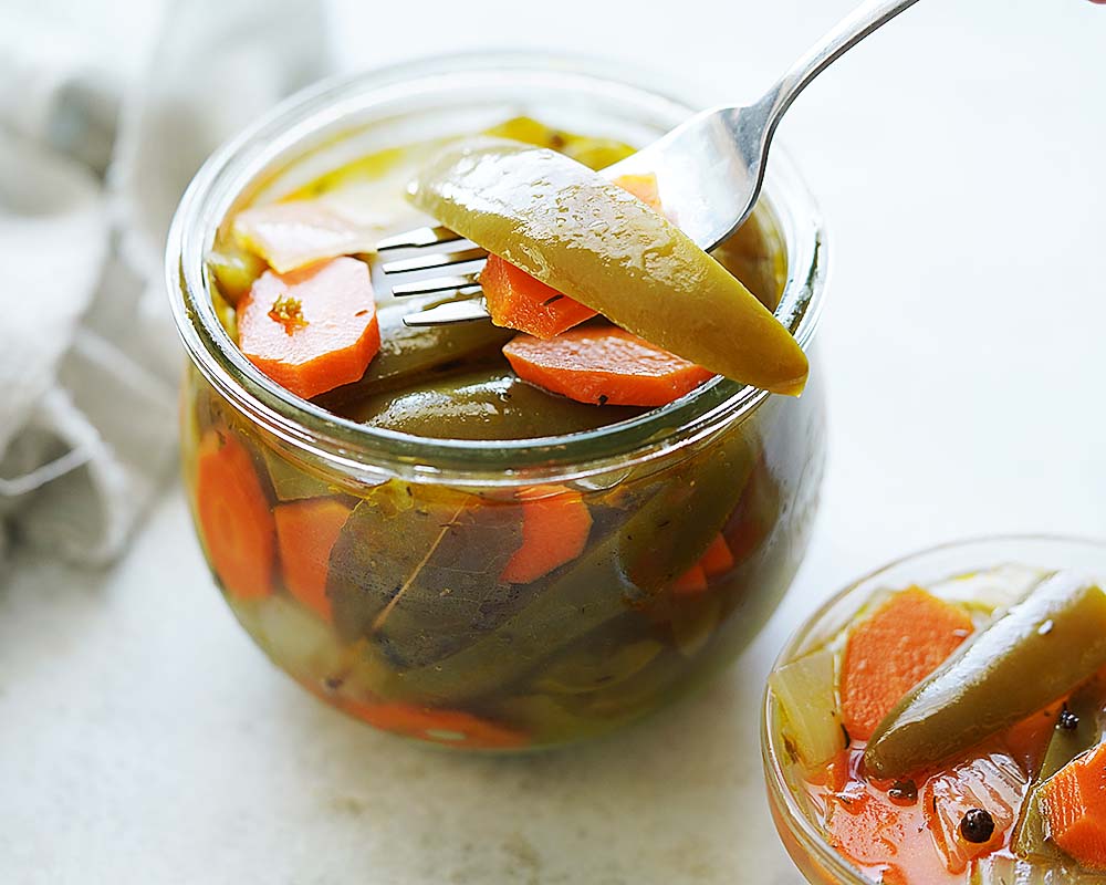 Pickled chiles and carrots in a small jar with a fork.