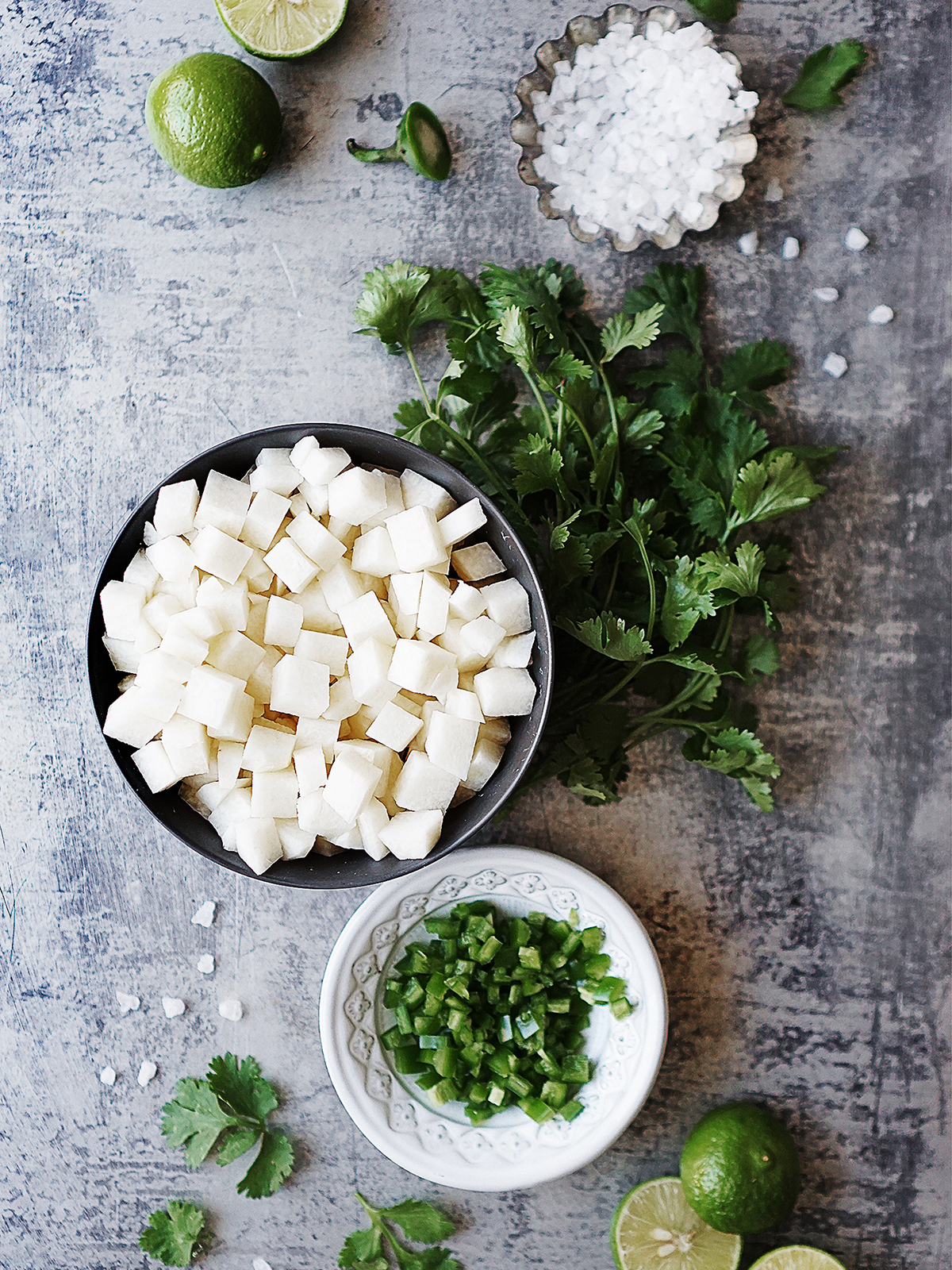 Ingredients in small bowls: jicama chunks, chopped jalapeño, cilantro, salt & limes.