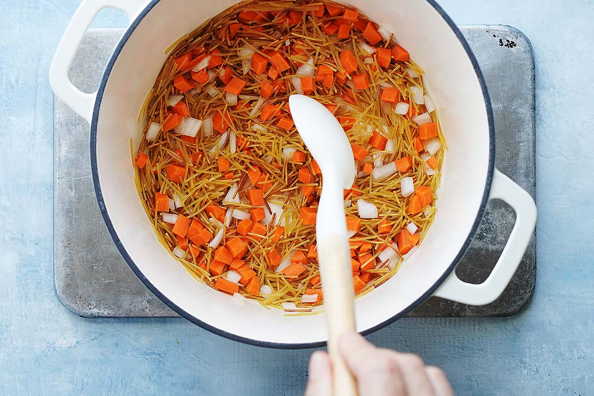 Cooking pasta, carrots & onions in a white pot.