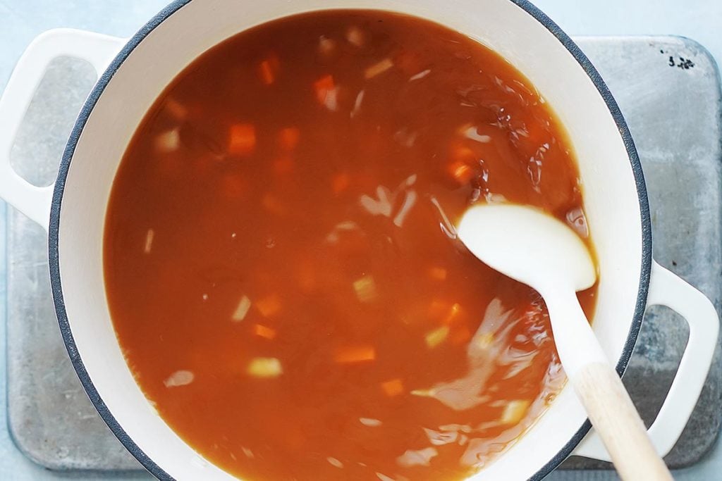 Mixing soup with a spoon in a white pot.