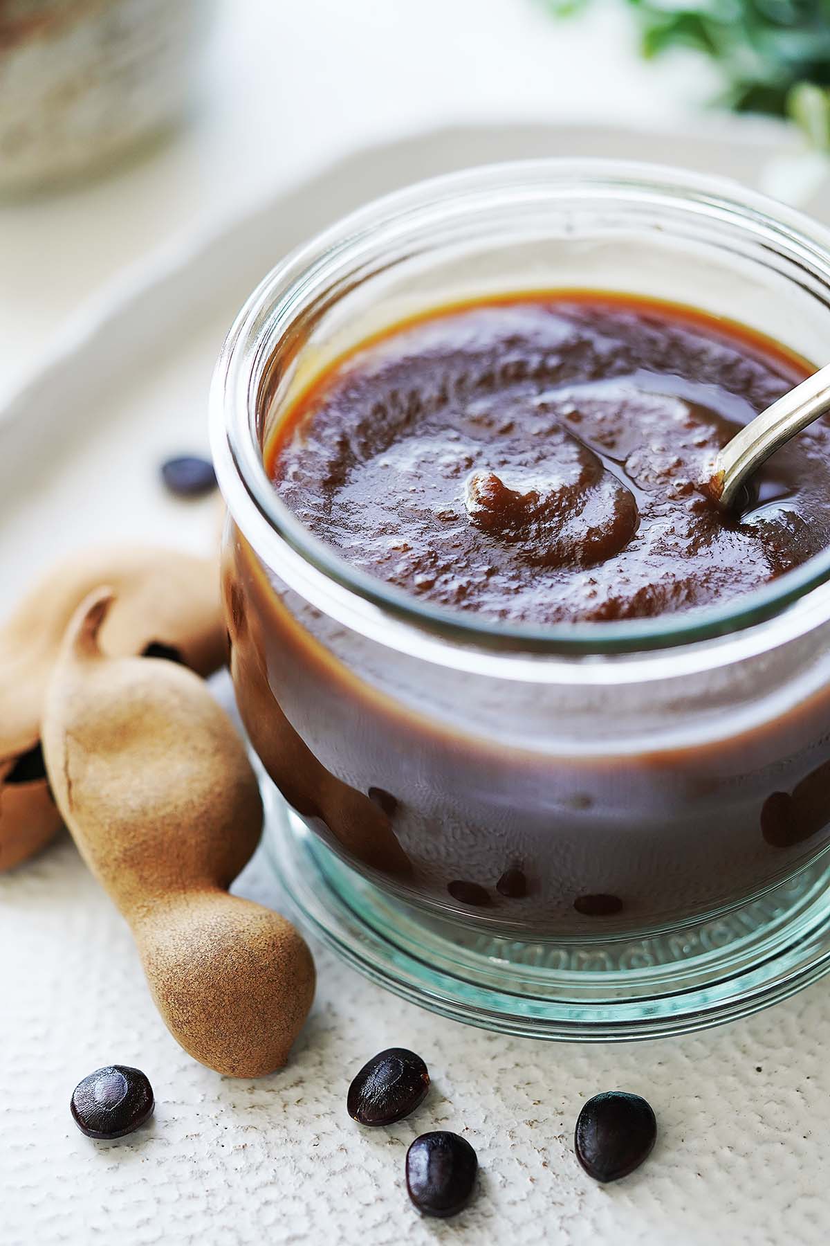 Tamarindo Paste in a small glass jar and whole tamarind pods on the side.