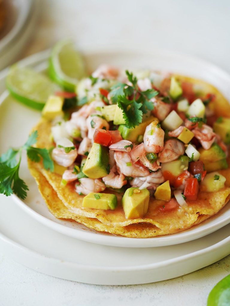 a tostada with shrimp and veggies on a white plate.