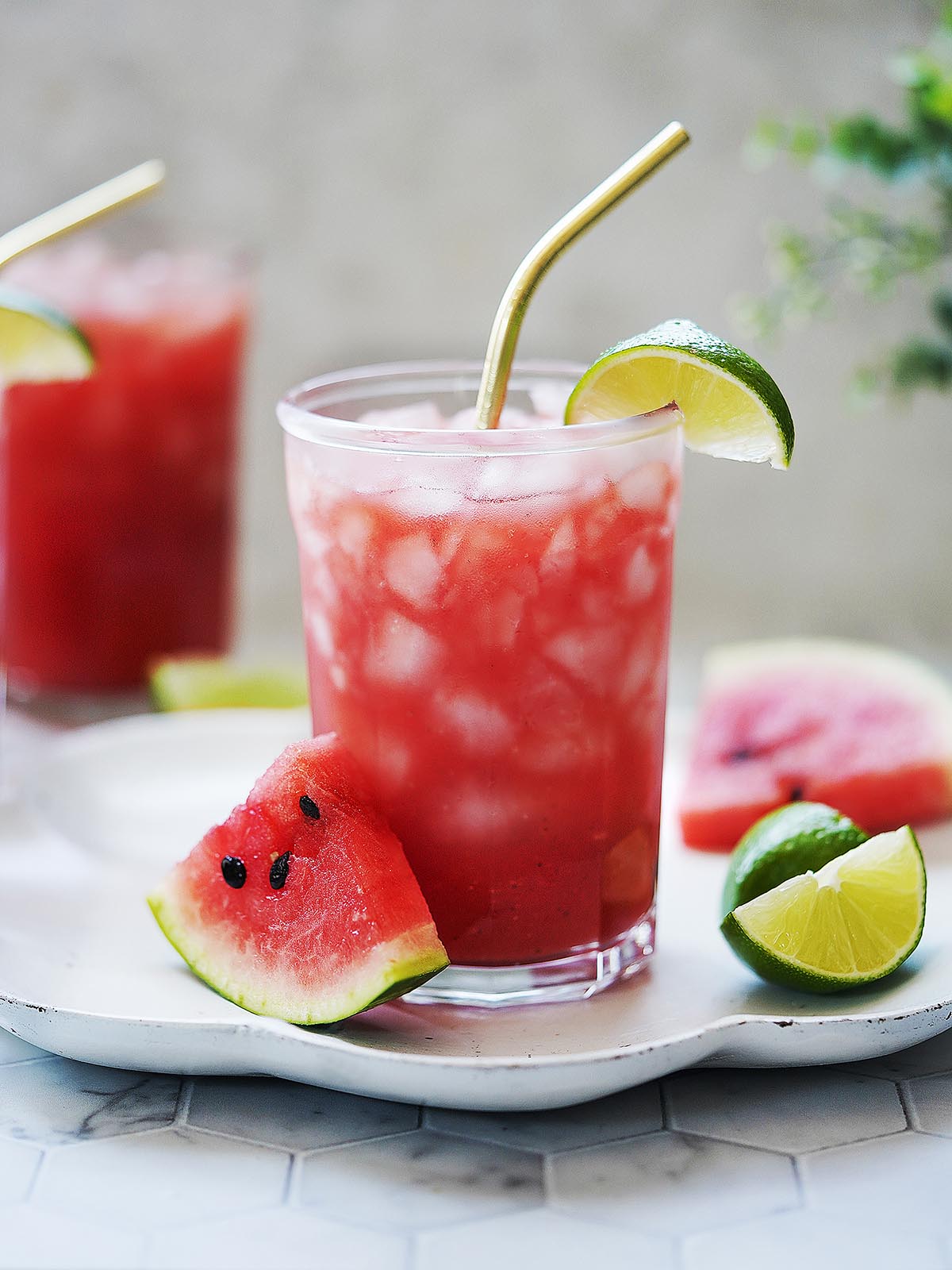 Two glasses filled with ice and watermelon juice with limes on the side.