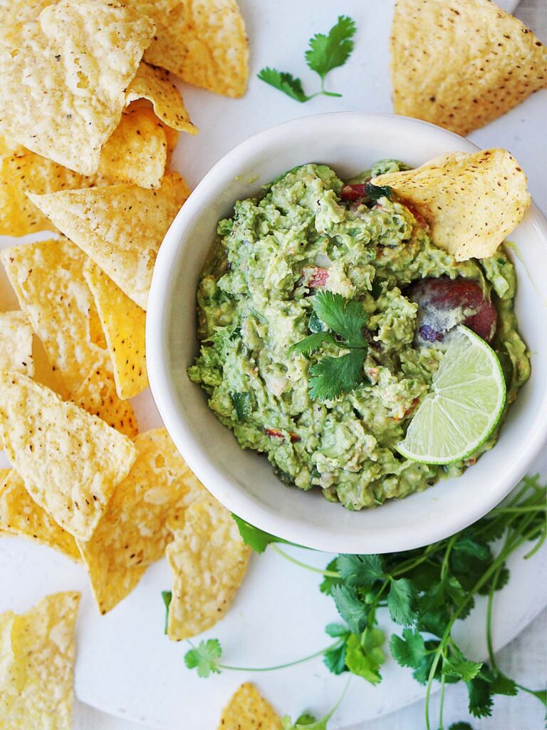 A white bowl with guacamole and chips on the side.