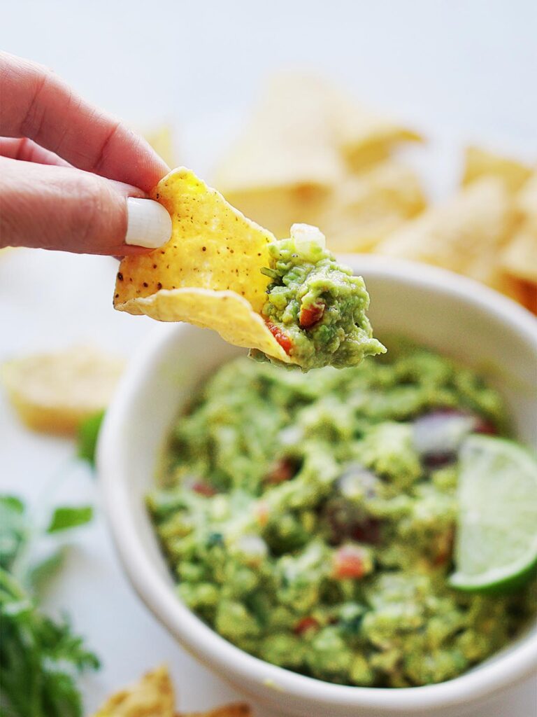 A hand with a tortilla chip and guacamole on top.