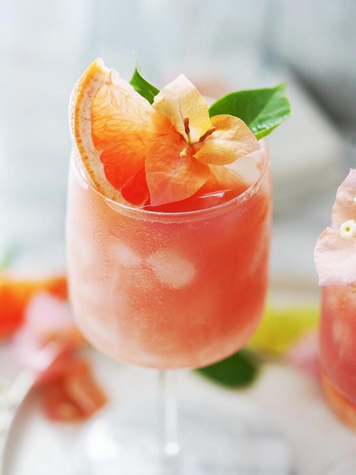 A Paloma cocktail garnished with grapefruit and an orange flower.