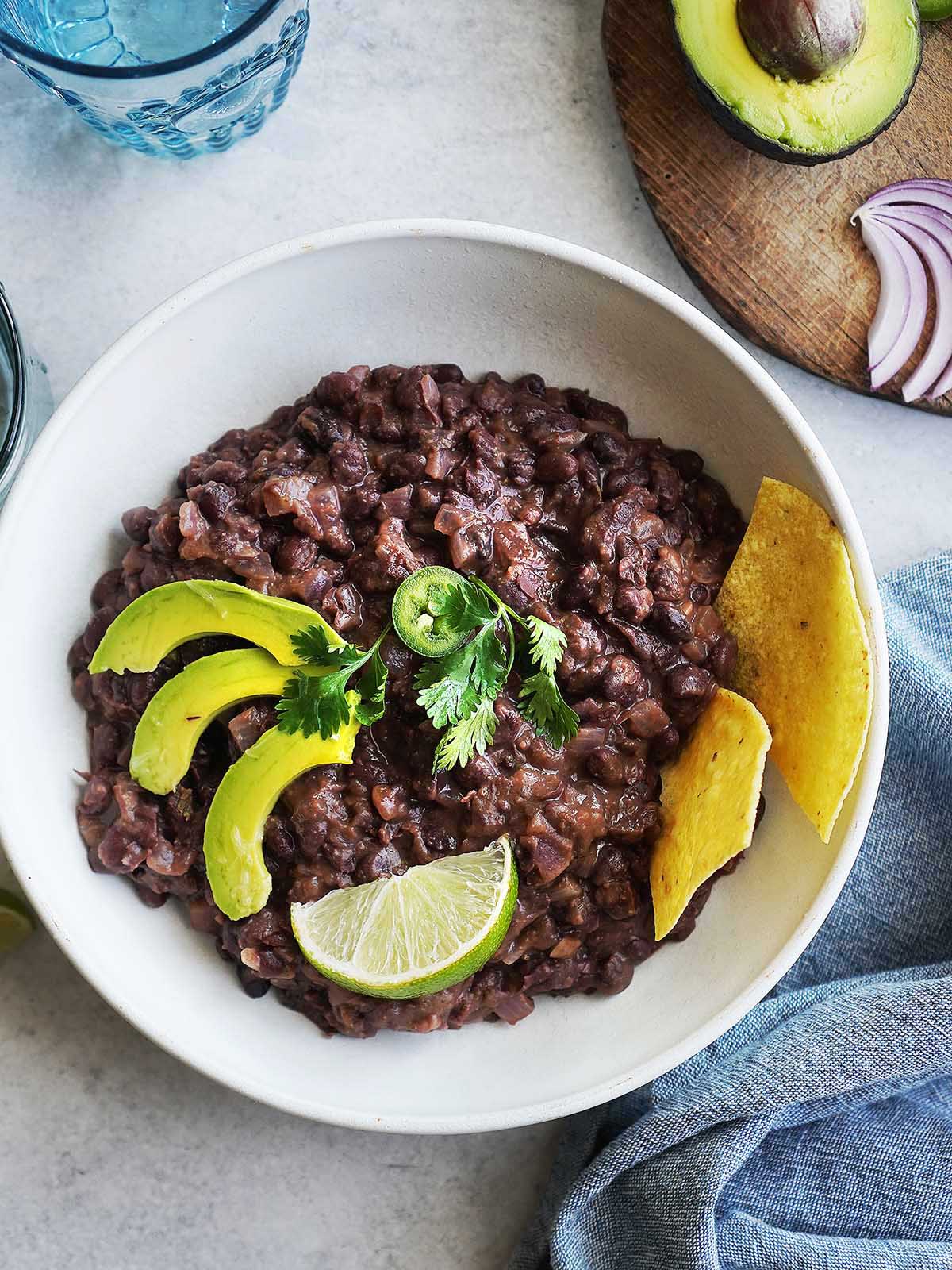 A bowl refried black beans garnished with avocado and tortilla chips.