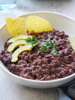 A bowl of black beans with chips on the side.