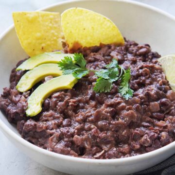 A bowl of black beans with chips on the side